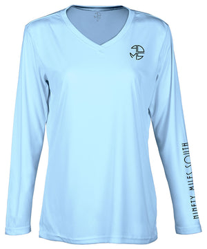 front view of a ladies light blue v-neck performance shirt with 90 Miles South Round left chest logo and right sleeve copy saying “90 Miles South”